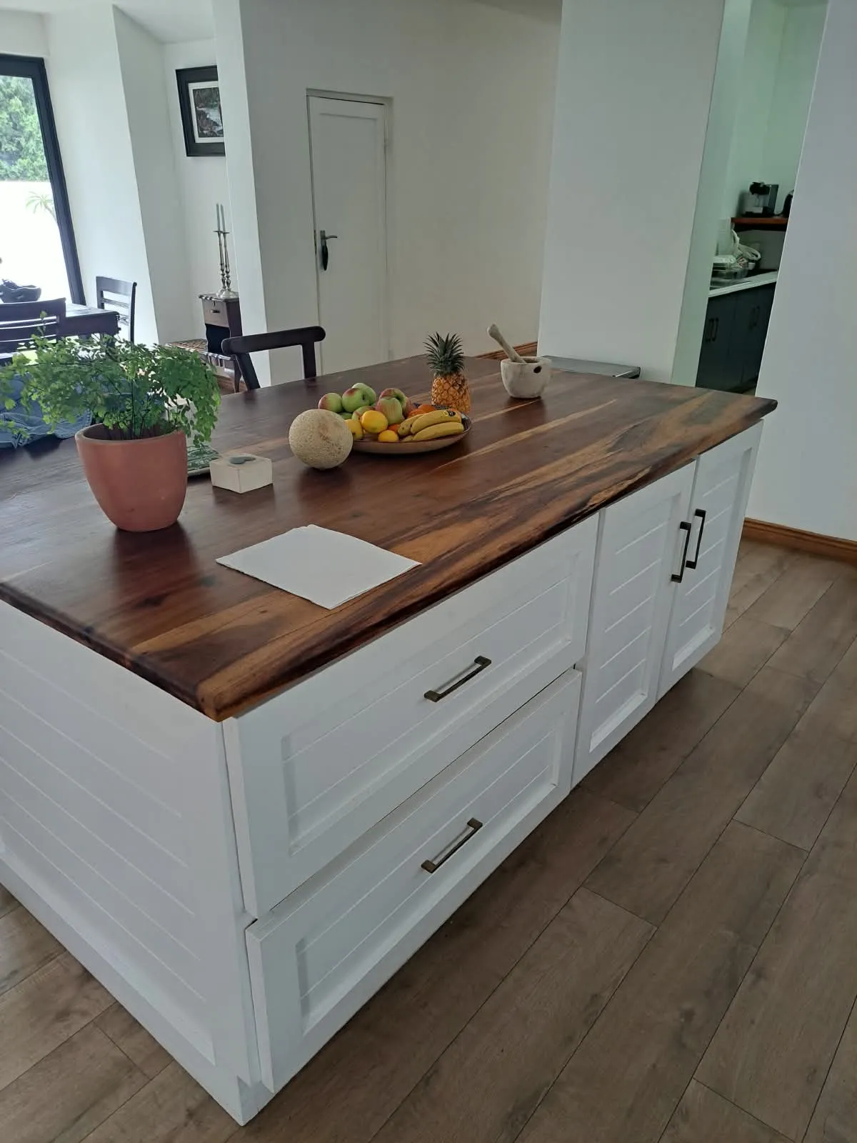 A kitchen island with a dark hardwood top and white panelled drawers and doors