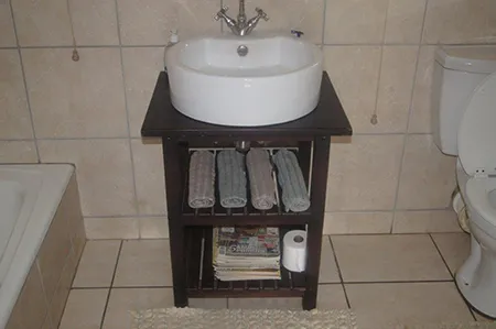 A dark timber stand holding a round basin, with slatted shelves for towels below