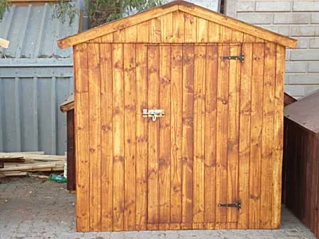 A small stained timber townhouse toolshed with a single door and a pitched roof