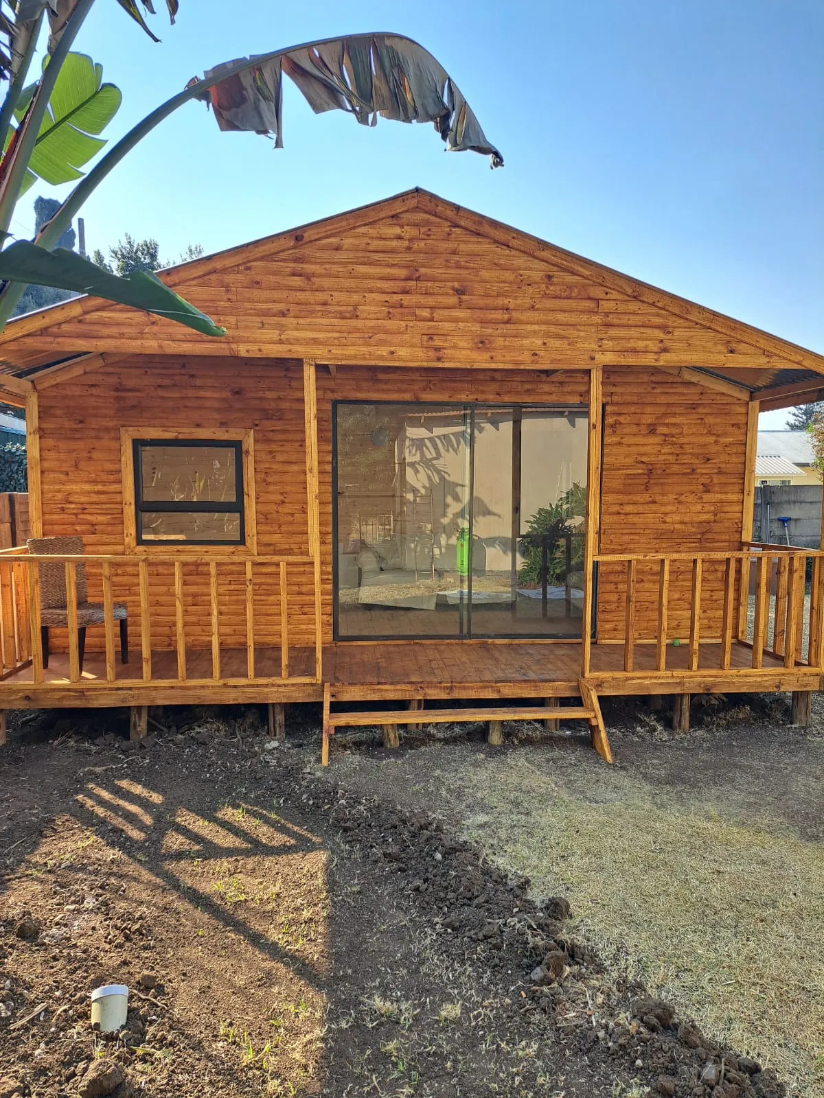 A timber wendy house with a veranda, a sliding glass door and a window, in a garden