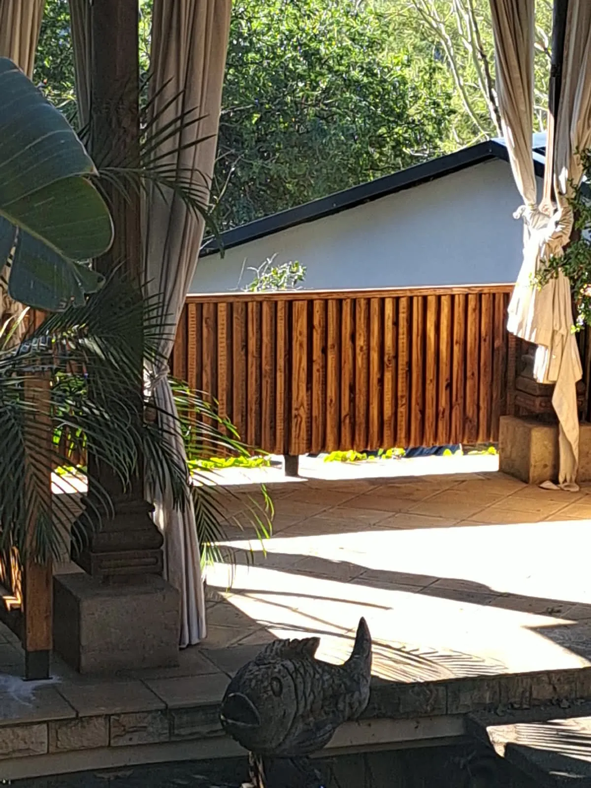 A stained wooden fence made of vertical boards, seen between curtains on a patio